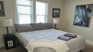Quarto com uma cama, duas mesas de cabeceira com luminárias, um ventilador de teto e um quadro abstrato grande na parede.