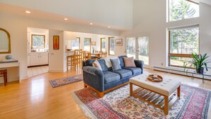 A spacious living room with a blue sofa, a wooden coffee table, and a dining area with a table and chairs. - Peaceful Vermont Hideaway Near Stowe | Wooded View (Elmore)