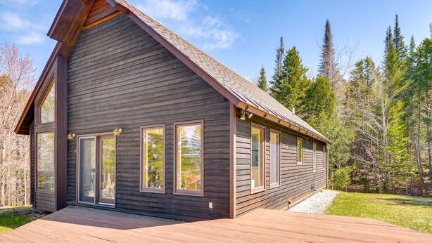 A modern log cabin with large windows, a wooden deck, and a forest backdrop. - Peaceful Vermont Hideaway Near Stowe | Wooded View (Elmore)