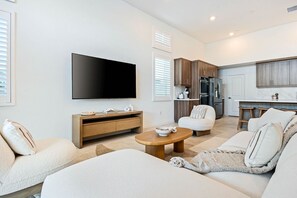 Een moderne woonkamer met een flatscreen televisie, een bank, een salontafel en een keukenhoek met kasten en apparatuur.