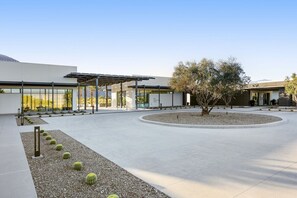 Un bâtiment moderne doté d’une allée couverte, d’un jardin circulaire agrémenté de cactus et surplombé d’un ciel dégagé.