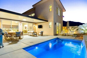 Ein modernes Haus mit Swimmingpool, Sitzgelegenheiten im Freien und einer flachen Dachkonstruktion.