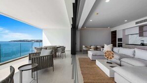 Ett modernt vardagsrum med en soffa, ett soffbord och en matplats, med utsikt över ett vackert hav.