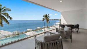 En modern balkong med utsikt över havet, en pool och utomhusmöbler.