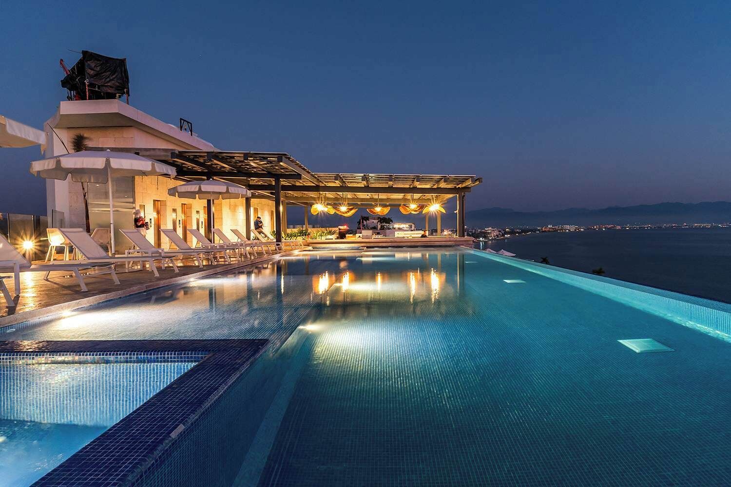 Una piscina infinita con vistas al mar, un área de estar cubierta y sillones de descanso.