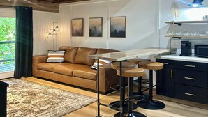 A modern kitchen with a bar area, a brown leather sofa, and a dining table with bar stools.