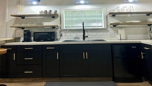 A modern kitchen with black cabinets, a microwave, a coffee maker, and a sink. There are three pendant lights above the counter.