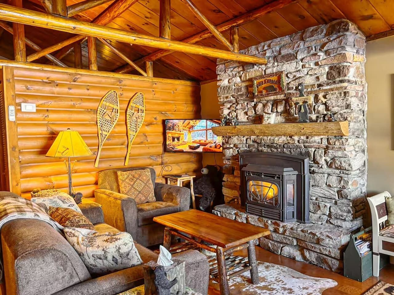 L’intérieur chaleureux d’un chalet en rondins, avec une cheminée en pierre, des murs en bois et un coin salon confortable.