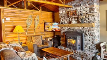 L’intérieur chaleureux d’un chalet en rondins, avec une cheminée en pierre, des murs en bois et un coin salon confortable.