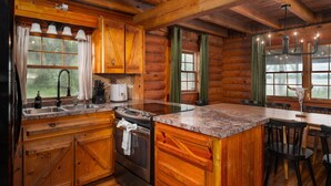 Interior rústico de una cabaña de troncos con muebles de madera, encimera de granito, fregadero, estufa y comedor con sillas.