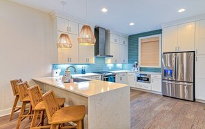 A modern kitchen with white cabinets, a central island with bar stools, stainless steel appliances, and a blue-tiled backsplash. - Rosé All Day • Insta • 21 Beds • Hot Tub/Game Room (Nashville)