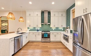 A modern kitchen with white cabinets, stainless steel appliances, and a green tiled backsplash. - 18 Beds Hot Tub Pool Table Bunk Room (Nashville)
