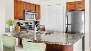 A kitchen with wooden cabinets, stainless steel appliances, granite countertops, and a built-in island with seating. - Spacious 1-bedroom 1 bath villa with full kitchen beautiful Orlando with AC (Orlando)