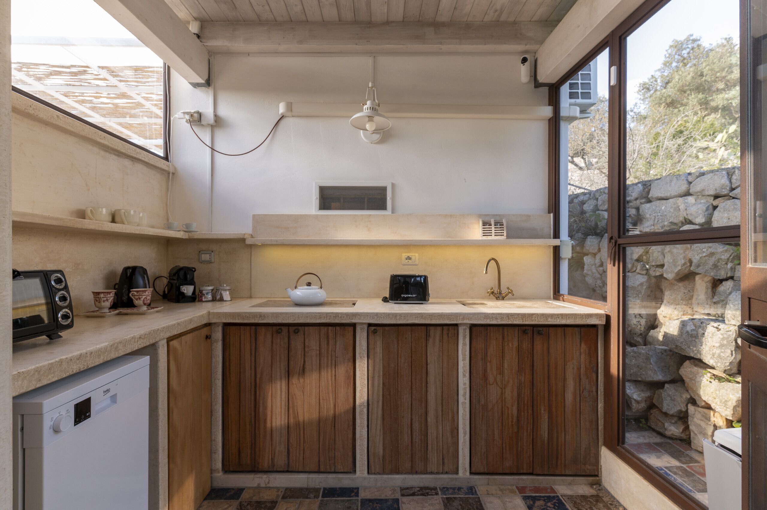 Una cocina compacta con armarios de madera, lavavajillas integrado, cafetera y hervidor.