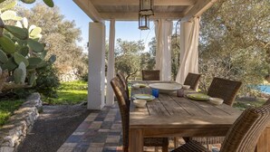 Un espace extérieur abrité, aménagé pour les repas, avec une table en bois, des chaises en osier et une lanterne.