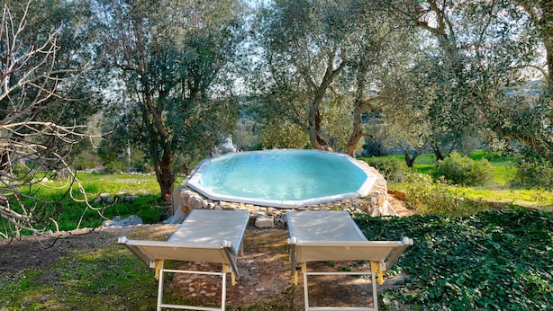 Un bain à remous entouré d’arbres et de verdure, avec deux chaises longues au premier plan.