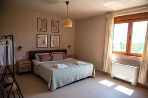 Une chambre à coucher comprenant un lit, des tables de chevet, un radiateur, une fenêtre avec des rideaux et des œuvres d’art murales.
