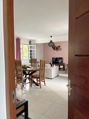 A modern living room with a dining area, a television, and a pink wall. - For an unforgettable stay (La Trinité)