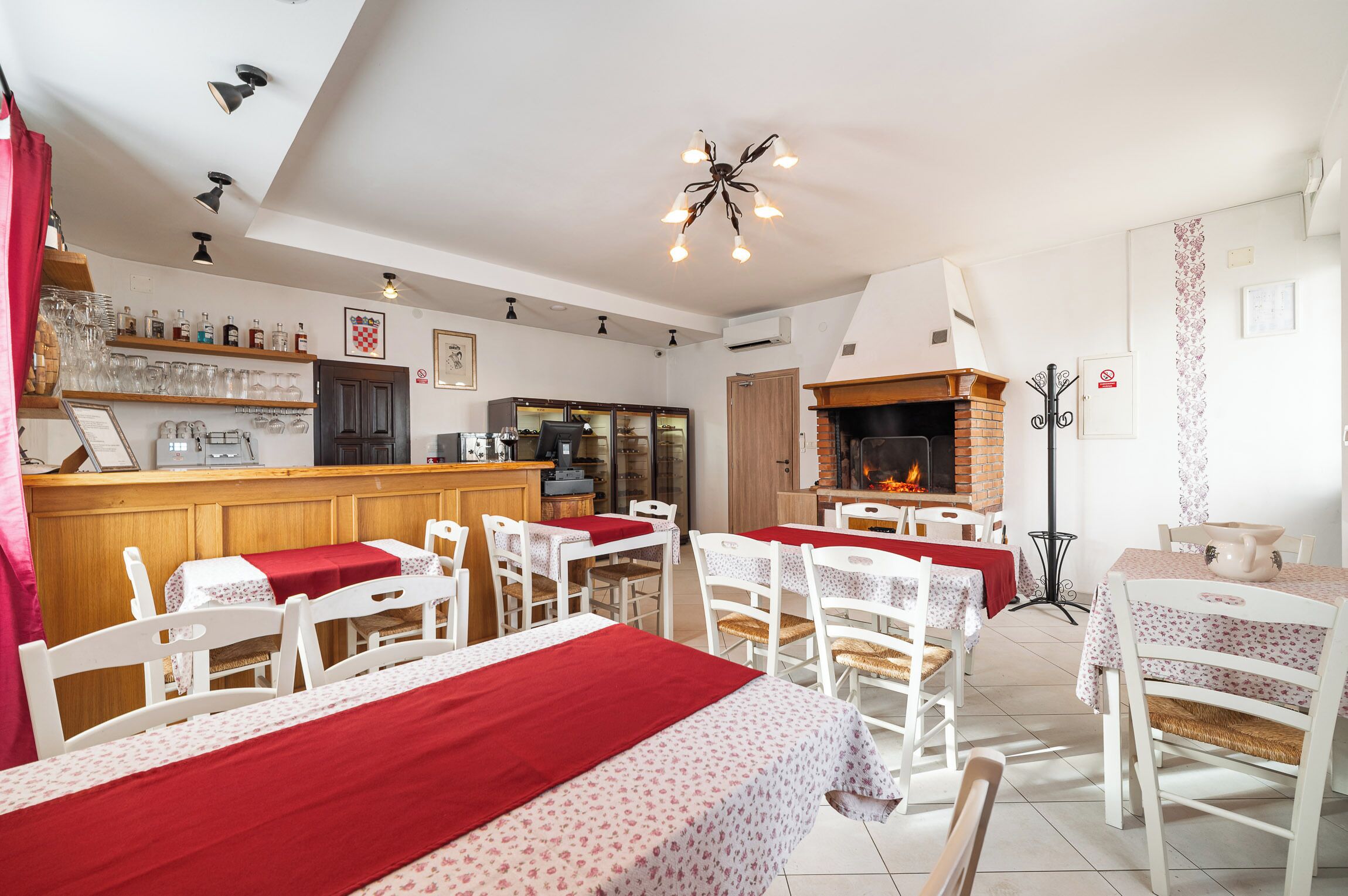 A cozy dining area with tables and chairs, a bar area with shelves of bottles, and a fireplace.