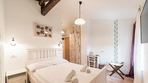 Una cama bien hecha con sábanas y toallas blancas, un cabecero de madera, una mesita de noche pequeña y un aplique en la pared.
