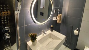 Et moderne badeværelse med et stort spejl, håndvask, bruser og toilet.