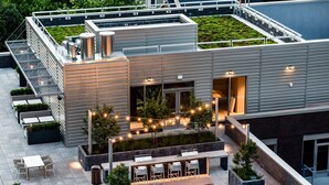 Um terraço no telhado com área de estar externa, bar e escadaria para um andar superior.