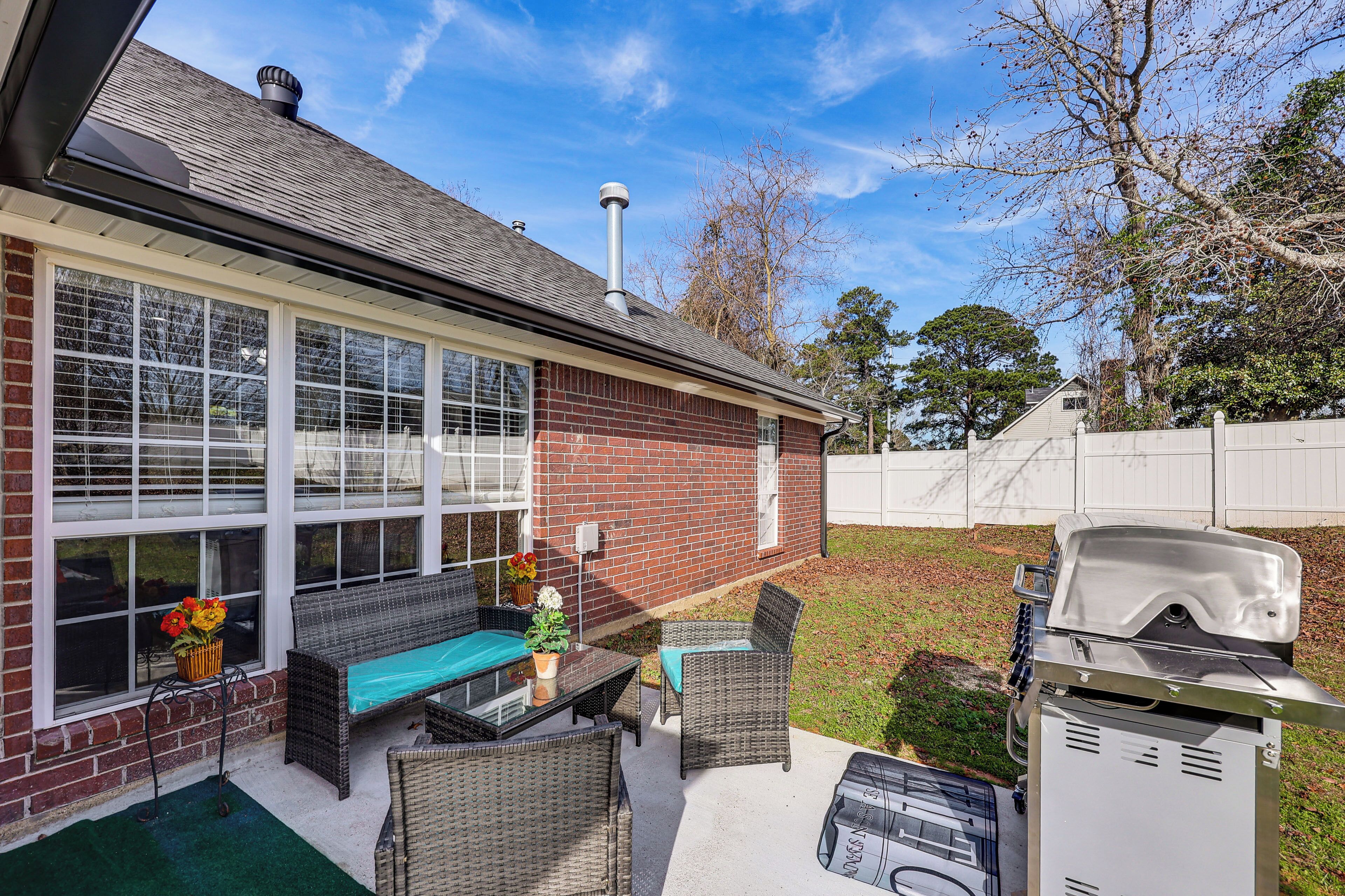A patio with wicker furniture, a grill, and a brick house.