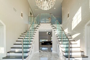 A grand staircase with glass railings leading to a second floor. - Expansive Riverside Mansion! Luxe, Family Friendly (Riverside)