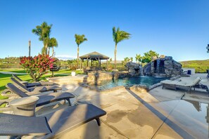 Un espace piscine comprenant des chaises longues, un kiosque et une cascade décorative.
