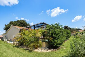 A modern house with a large glass extension, surrounded by lush greenery and a clear blue sky. - Golf, Dine & Relax Poolside! The Villages Retreat (The Villages)