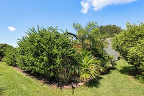 A well-maintained garden with various shrubs and a palm tree, a clear sky, and a building in the background. - Golf, Dine & Relax Poolside! The Villages Retreat (The Villages)
