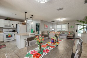 A modern kitchen with white appliances, a dining area with a wooden table, and a living room with a sofa and a plant. - Golf, Dine & Relax Poolside! The Villages Retreat (The Villages)