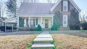 A two-story house with a covered porch, a front yard with a stone pathway, and a brick chimney.