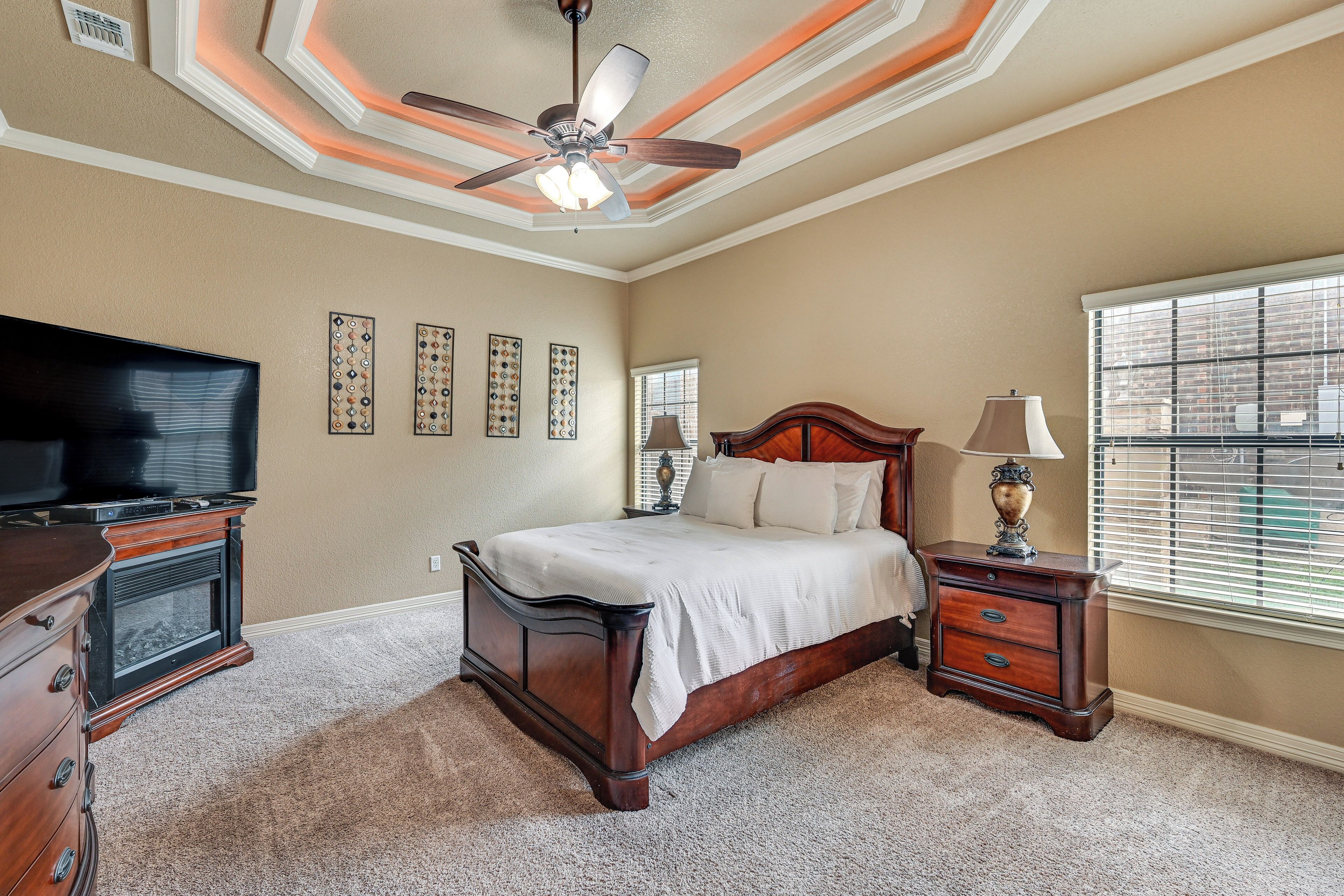 A bedroom with a bed, dresser, TV, and a ceiling fan.