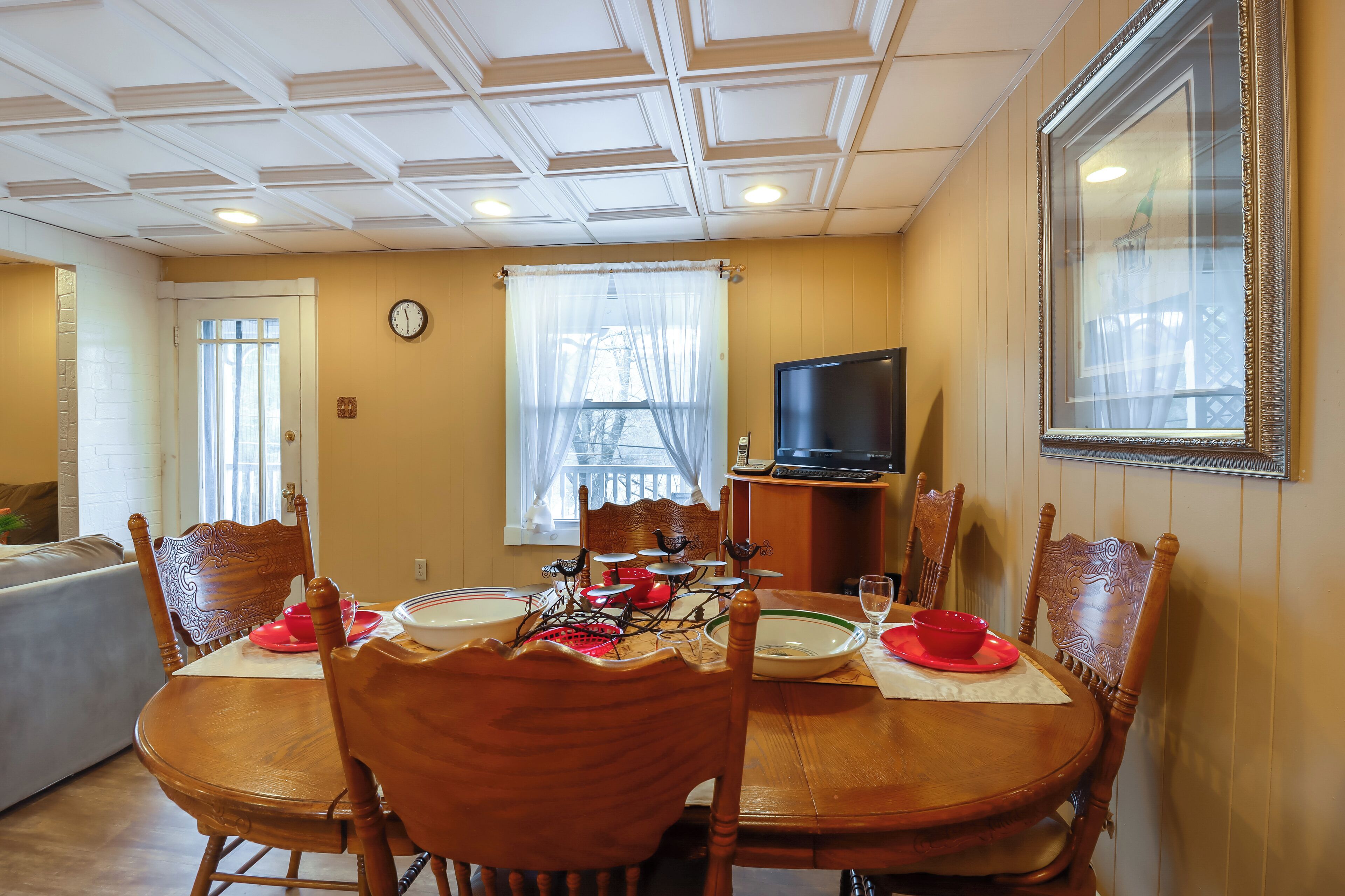A dining area with a wooden table, chairs, and a television on a stand.