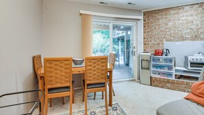 Cozinha compacta com parede de tijolos, área de refeições com mesa e cadeiras, e uma porta de vidro deslizante que dá para área externa.