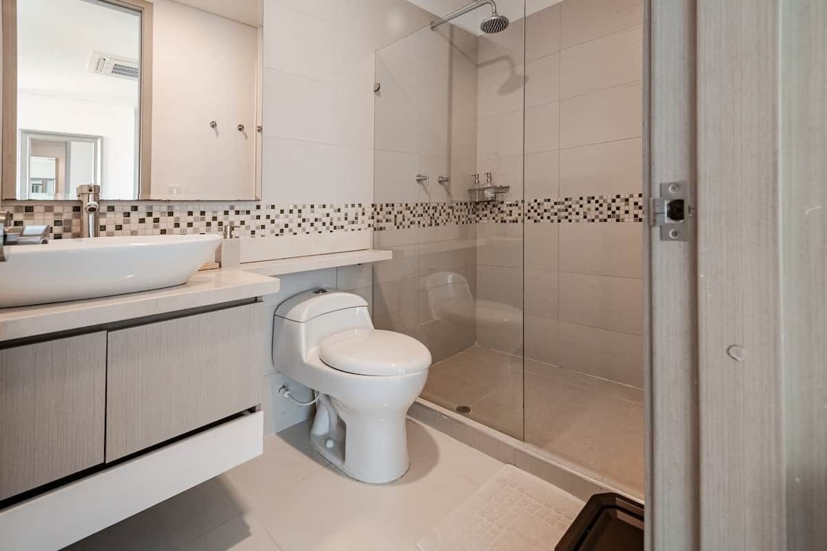 A modern bathroom with a glass-enclosed shower, a white toilet, and a large mirror above the sink.
