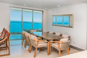 A dining area with a large table and chairs, a view of the ocean through glass doors, and a framed window on the wall. - Super Luxury Beachfront 4BR w/ Ocean view Balcony (Cartagena)