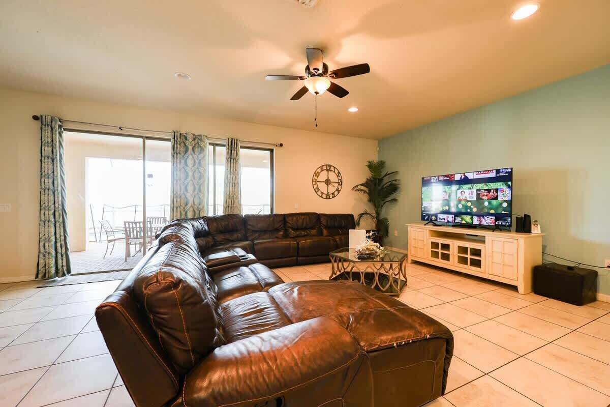 Una sala de estar con un sofá modular, un ventilador de techo, un televisor y un comedor con sillas.