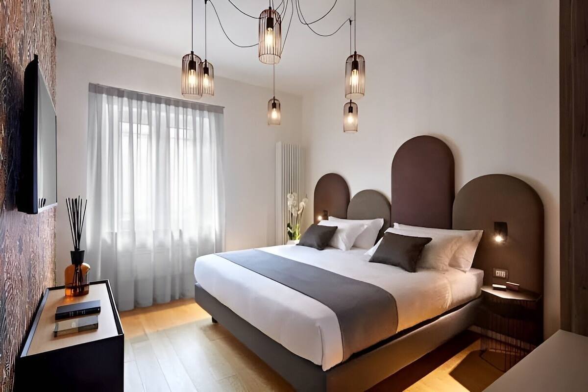 A modern bedroom with a large bed, bedside tables, a TV, and a window with curtains.