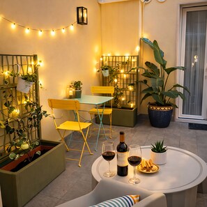 A cozy outdoor seating area with yellow chairs, a table with wine glasses and a bottle, string lights, and potted plants. - Casa Flora Verona (Verona)