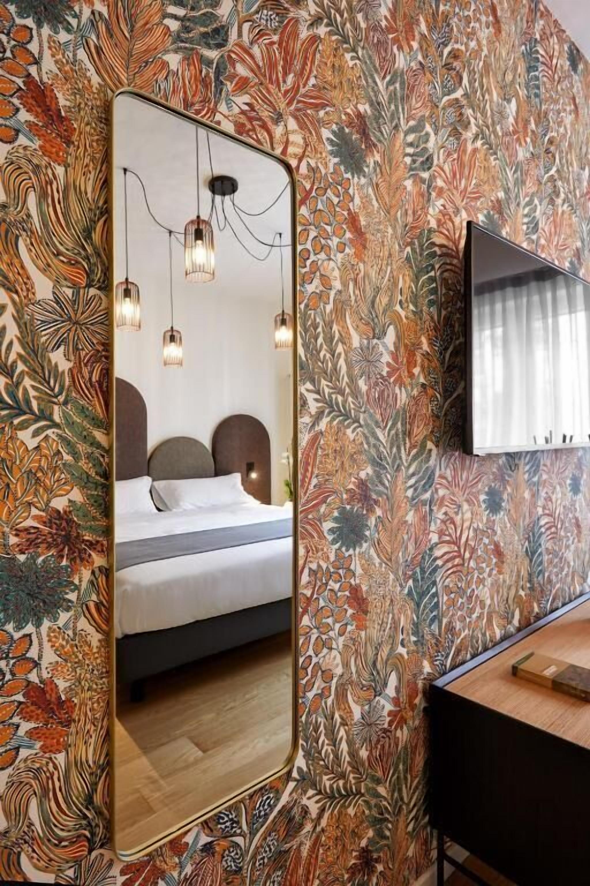 A bedroom with a large mirror, a bed with pillows, a nightstand, and a wall-mounted TV.
