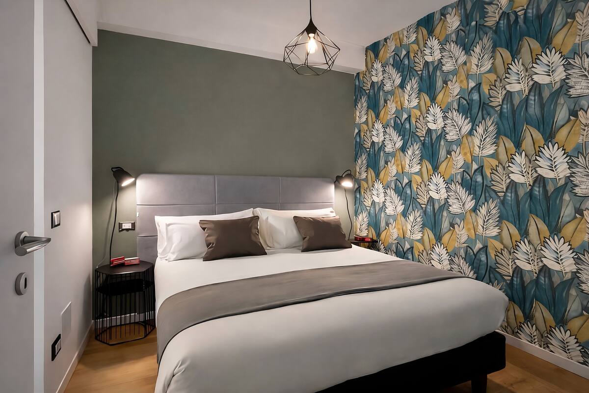A modern bedroom with a large bed, a headboard, bedside tables, and a wall with a leaf pattern.
