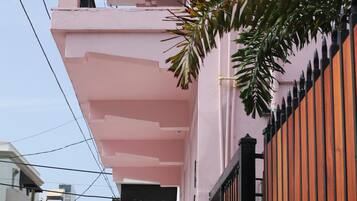 A pink building with a balcony, a gated entrance, and parked cars along the street.