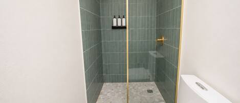 Et badeværelse med brusebad, toilet og en hylde med toiletartikler.