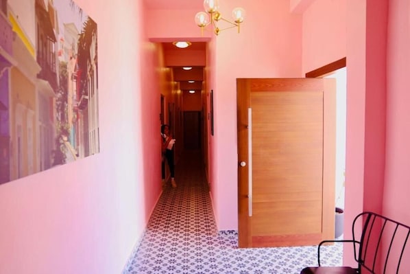 Un pasillo estrecho con paredes rosas, piso estampado y una puerta de madera.