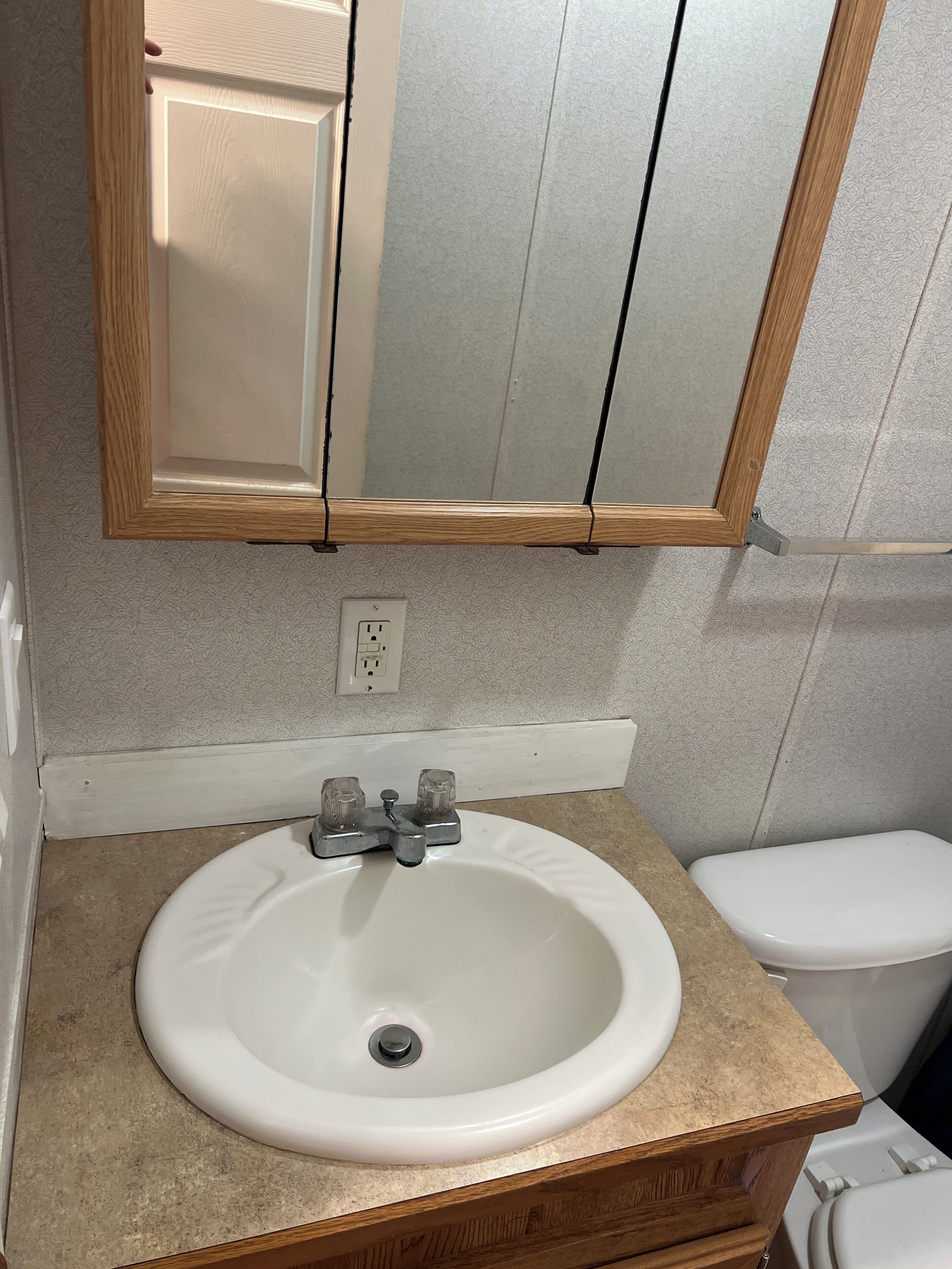 A bathroom with a white sink, wooden vanity, and a mirror above the sink.