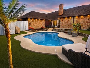 A backyard with a swimming pool, a brick house, and outdoor furniture. - 4-bedroom/Study/Sunroom/heated Pool house near Airport and Stadium (Irving)
