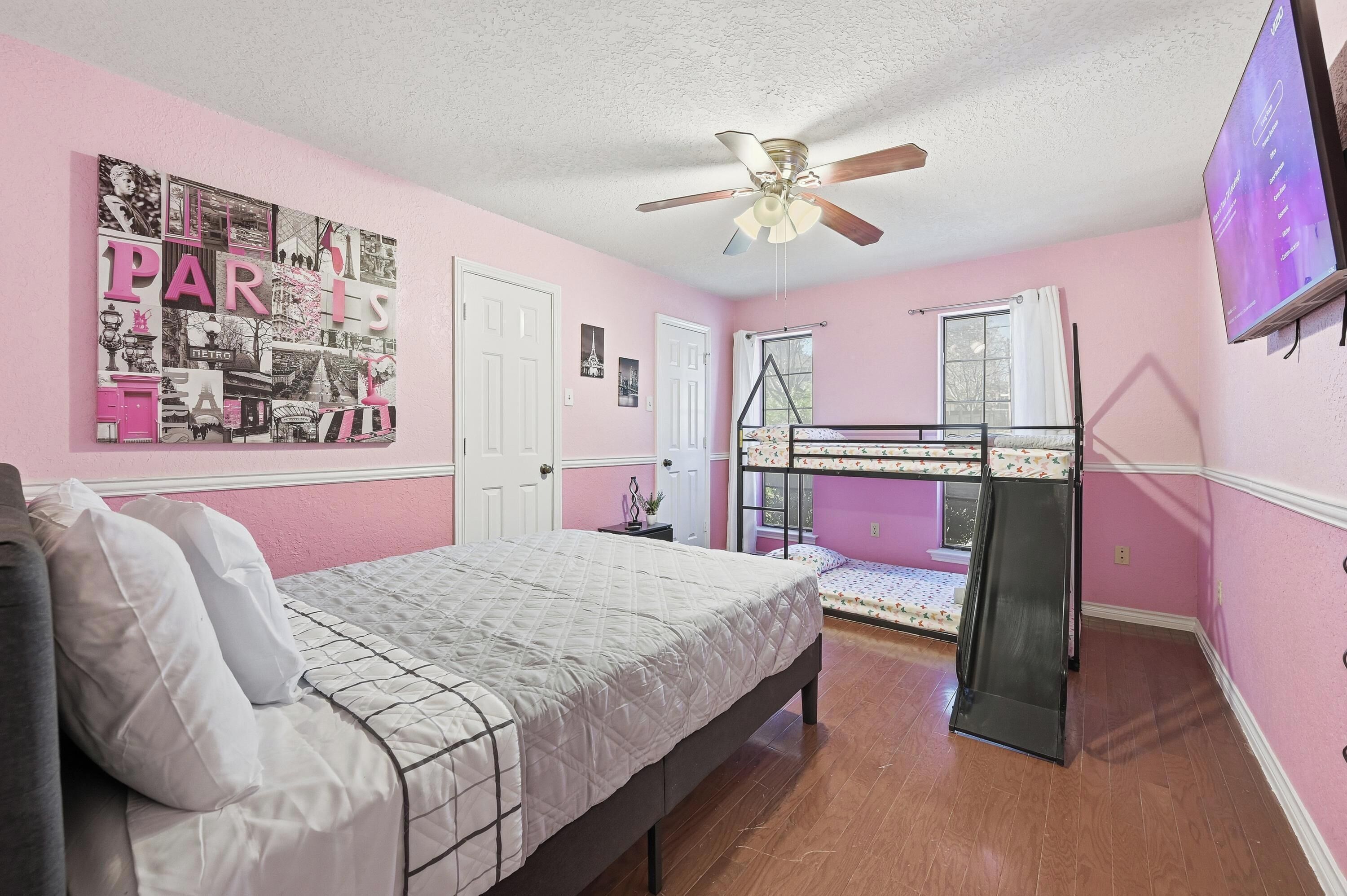 A bedroom with a bunk bed, a ceiling fan, a TV, and a poster on the wall.
