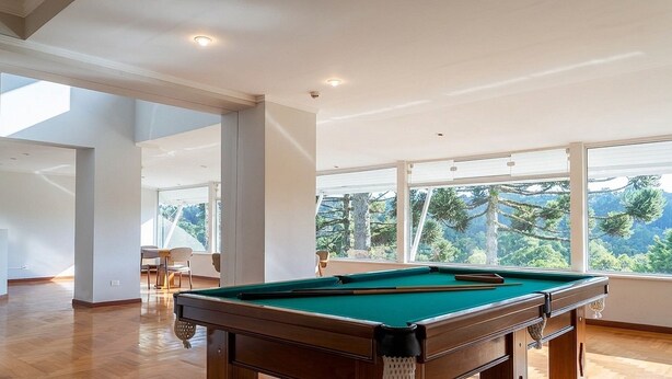Une table de billard se trouve dans une pièce spacieuse, dotée de grandes fenêtres qui offrent une vue sur les arbres et les montagnes.